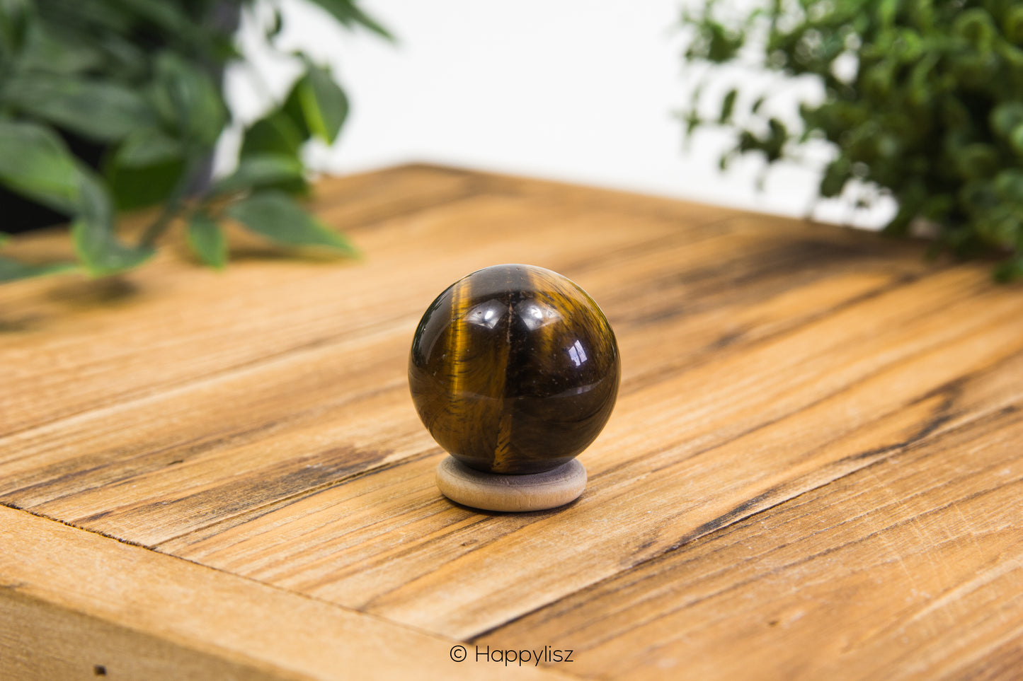 Tiger's eye crystal ball on a wooden surface with greenery in the background