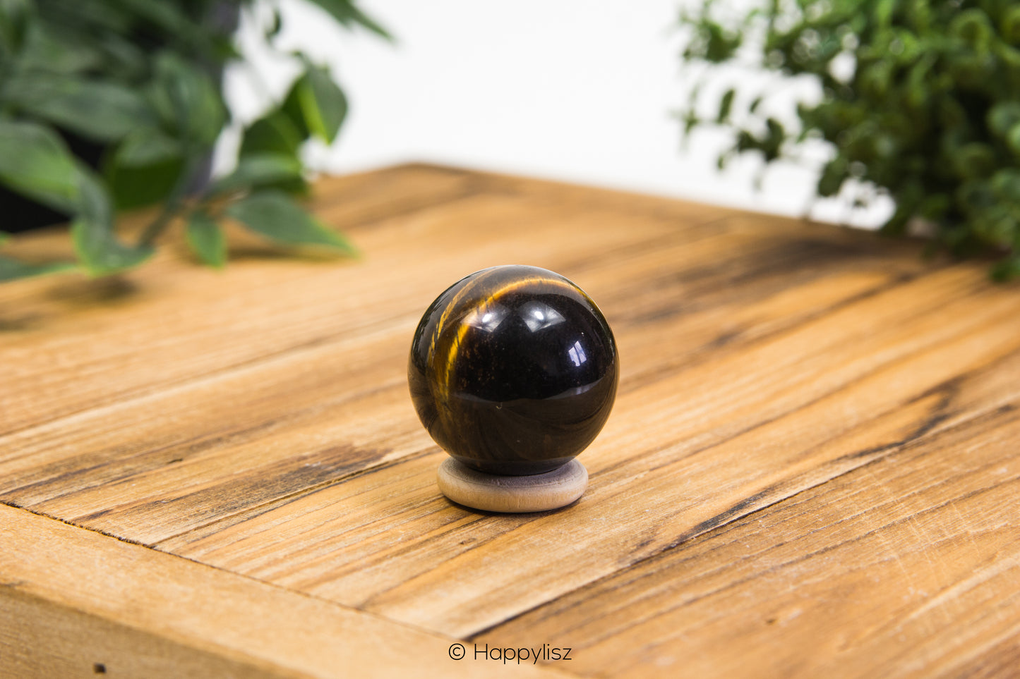 Black and gold spherical object on a wooden surface with greenery in the background