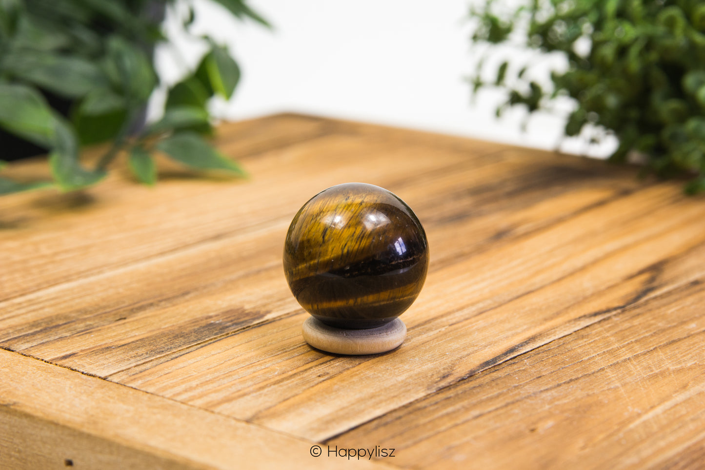 Tiger's eye crystal ball on a wooden surface with greenery in the background