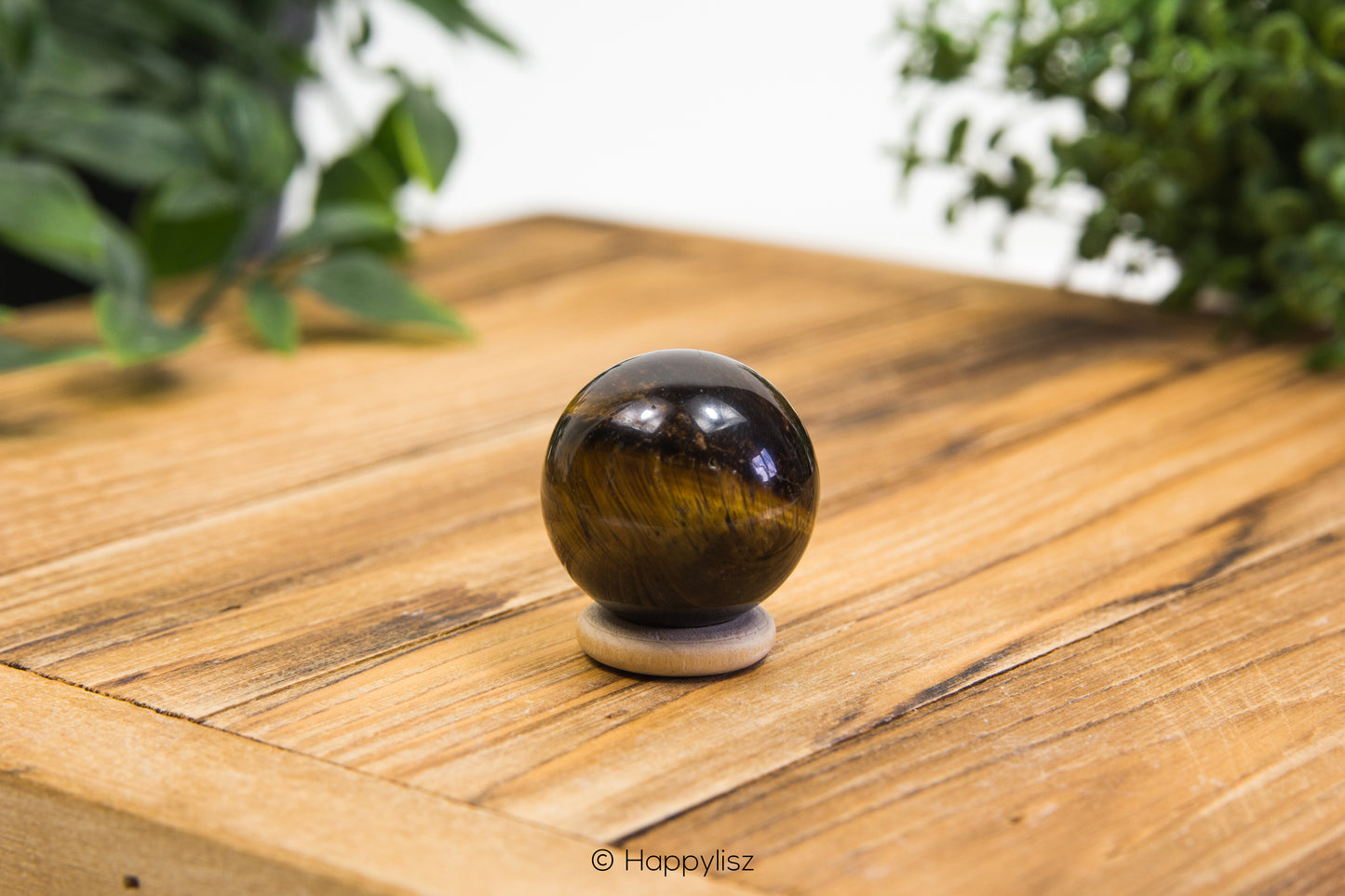 Tiger's eye crystal ball on a wooden surface with greenery in the background