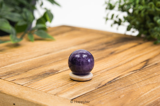 Amethyst crystal ball on a wooden surface with greenery in the background