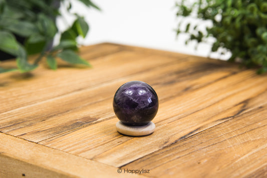 Purple crystal ball on a wooden surface with green plants in the background