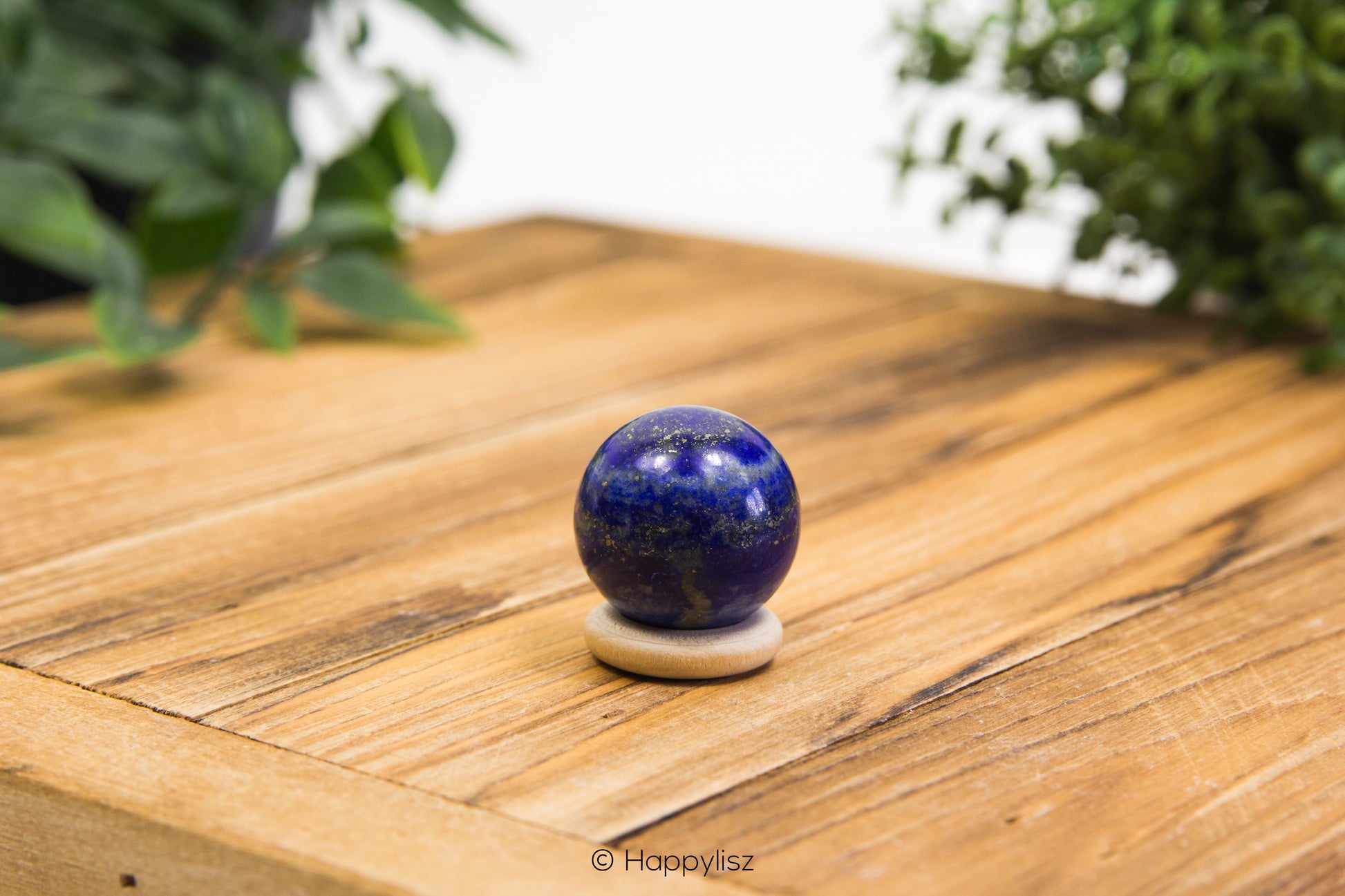 Blue spherical object on a white stand on a wooden surface with greenery in the background