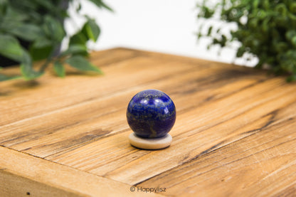 Blue spherical object on a white stand on a wooden surface with greenery in the background
