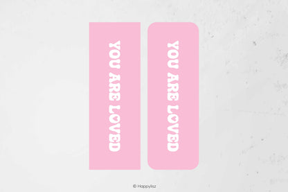 Two pink rectangular labels with rounded corners, each printed with the phrase 'YOU ARE LOVED' in white vertical text, shown on a light textured background.