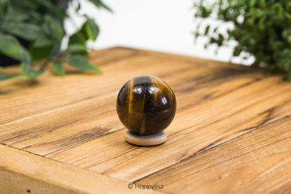 Tiger's eye crystal ball on a wooden surface with greenery in the background