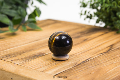 Black and gold spherical object on a wooden surface with greenery in the background