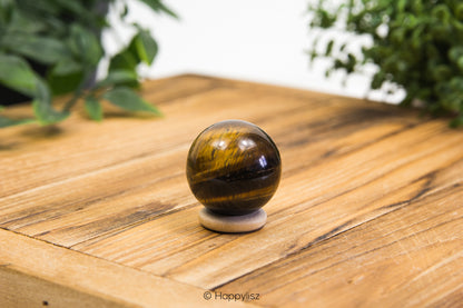 Tiger's eye crystal ball on a wooden surface with greenery in the background