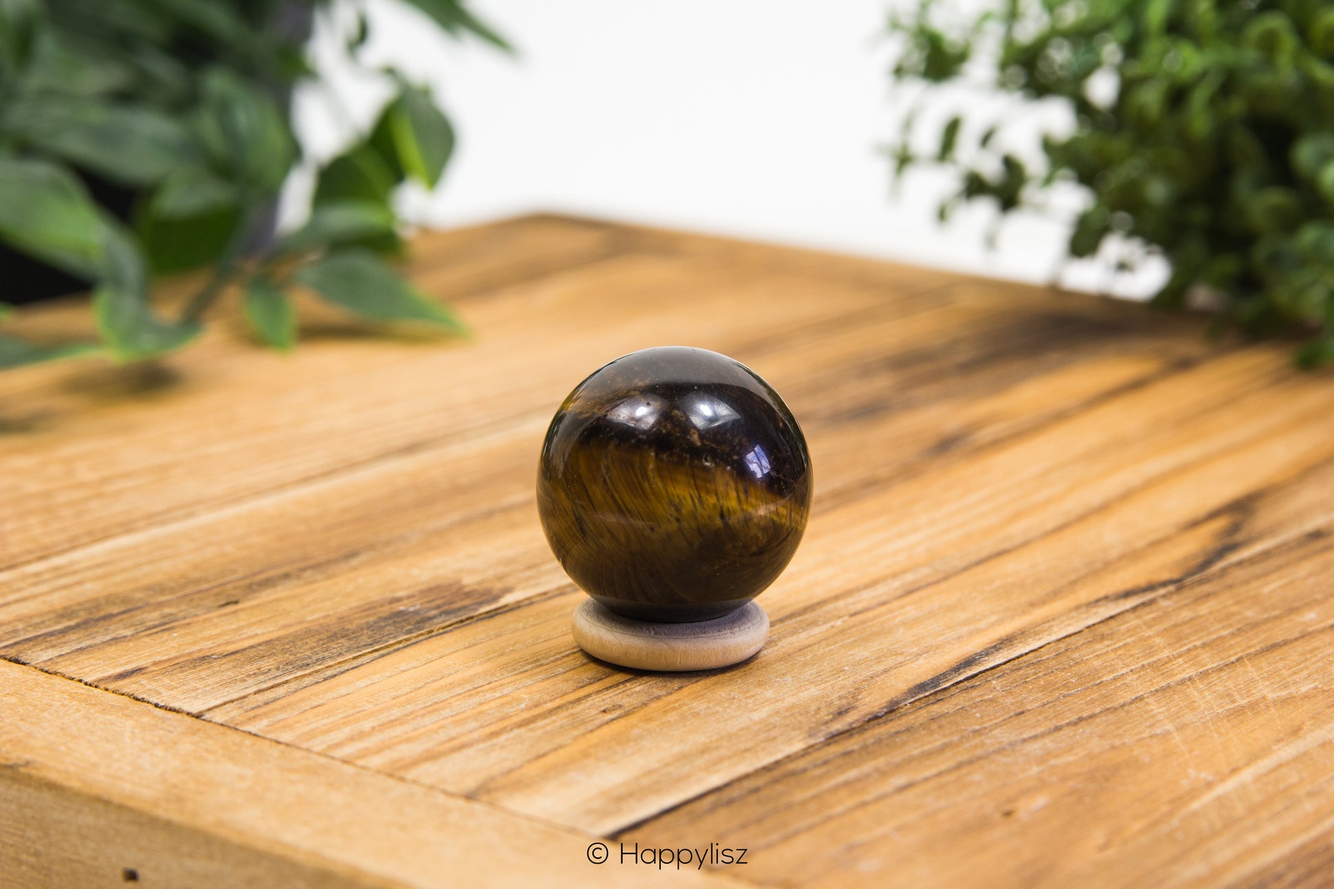 Tiger's eye crystal ball on a wooden surface with greenery in the background